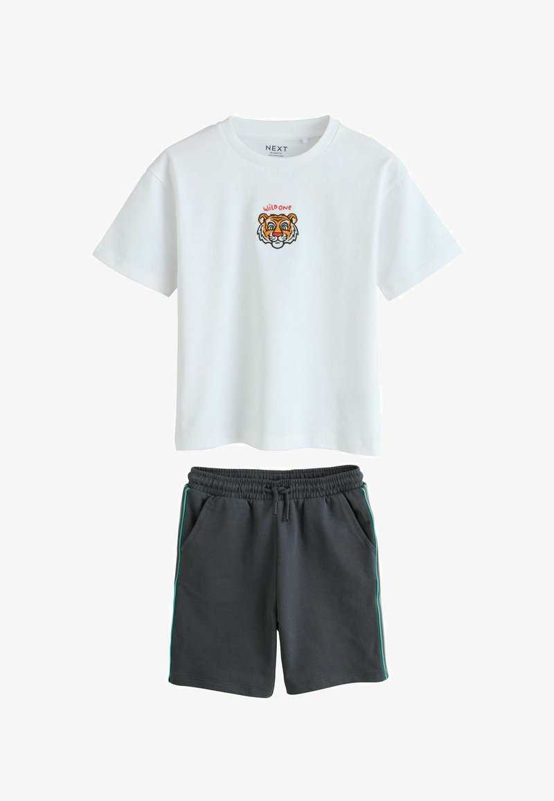 T-shirt blanc à manches courtes avec un petit visage de tigre et le texte « WILD ONE », associé à un short noir à cordon avec des bandes latérales.