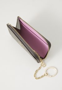 Portafoglio nero con texture, dotato di cerniera dorata e anello portachiavi a catena, con un interno viola. Il design aperto consente un facile accesso ai contenuti.