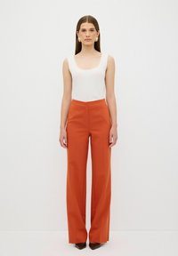 Brede oranje broeken van gladde stof, gecombineerd met een aansluitend wit geribbeld tanktop met een vierkante halslijn en dikke banden.