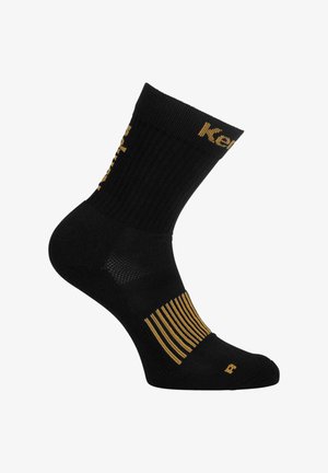 Zwarte sportsok met geribbelde textuur, verstevigde teen en hiel, gouden logo en accenten, met een patroonband vlak bij de boog.