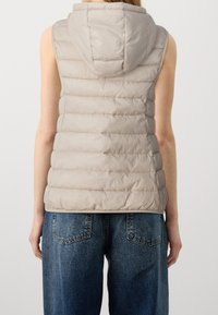 Veste matelassée sans manches de couleur beige avec capuche, présentant un design matelassé et une texture douce. Le dos est lisse avec un ourlet droit.