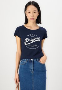 Marineblå bomull T-skjorte med korte ermer, med en hvit grafisk trykk. Sammen med en lyseblå denimskjørt som viser en klassisk passform.