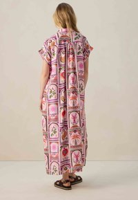 Robe maxi en tissu rose avec un motif floral vibrant. Manches courtes, coupe décontractée et fente jusqu'aux genoux. Associée à des sandales marron.