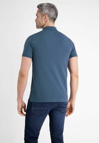 Ciemnoniebieska koszulka polo z krótkimi rękawami i klasycznym kołnierzykiem, o gładkiej fakturze i prostym dołem, noszona z ciemnymi dżinsami.
