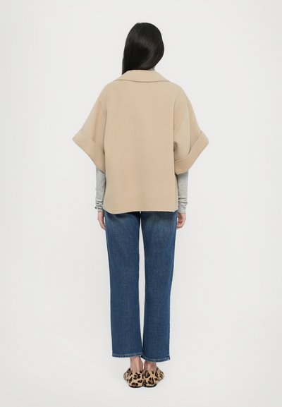 Beige knitted cape with a wide collar, paired with a gray long-sleeve top and blue straight-leg jeans. Leopard print slip-on shoes.