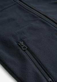 Giacca in pile nera con tasca con zip, texture liscia e design minimalista con un dettaglio zip in evidenza.