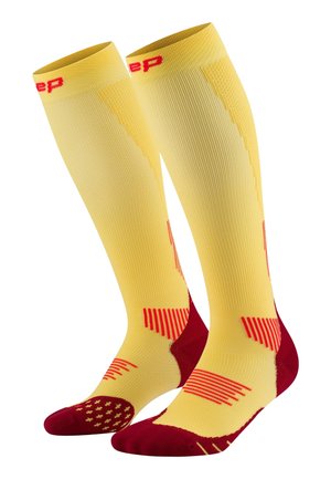 Yellow knee-high compression socks with red accents, featuring ribbed texture, dotted grip pattern at the toe, and horizontal stripes on the sides.