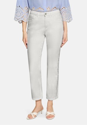 Weiße, verkürzte Hosen mit seitlichen Spitzendetails getragen zu einer hellblauen Bluse mit Lochspitzenärmeln und weißen Sandalen mit Absatz.