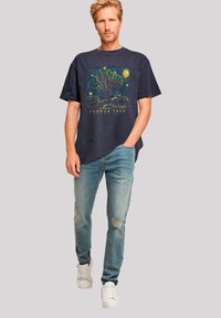 Maritimer Grafik-T-Shirt in Navy mit einem Design von Baum und Sonne, kombiniert mit hellblauen, abgewetzten Jeans und weißen Sneakern. Lässige Passform.