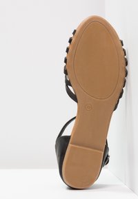 Black sandal with flat sole, featuring multiple strap details and a tan, textured rubber outsole. Size indicated as 38.