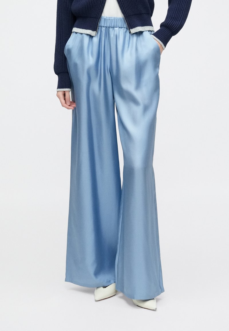 Pantalones anchos de satén azul claro con cintura elástica fruncida y bolsillos laterales, combinados con un cárdigan azul marino y tacones blancos.