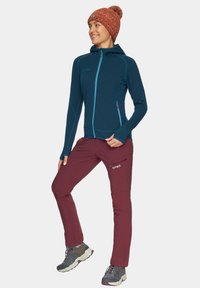 Ciemnoniebieska kurtka na zamek z kapturem, zestawiona z bordowymi spodniami z zasuwaną kieszenią. Szare buty trekkingowe z sznurówkami oraz fakturowana czapka dzianinowa.