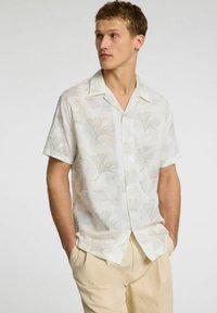 Kortærmet, lysefarvet button-up skjorte med blomstermønster, lavet af et tekstureret stof. Har en standard krave og afslappet pasform.
