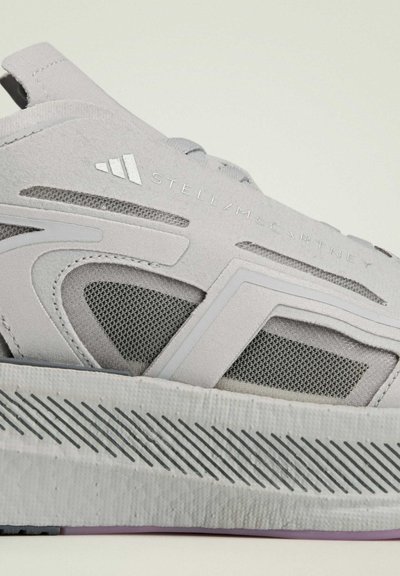 Chaussure de sport grise avec un design en couches, comprenant des panneaux en mesh et un matériau texturé. Comprend une semelle en caoutchouc avec des motifs en rainures et une marque.