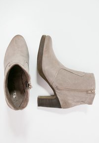Bottines en daim beige avec un petit talon empilé. Elles sont dotées d'une fermeture éclair sur le côté, d'un bout arrondi et de détails de couture subtils le long de la tige.