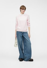 Maglione rosa chiaro, jeans in denim blu a gamba larga e scarpe platform nere chunky. Borsa bianca minimalista. Tessuto morbido, vestibilità comoda.