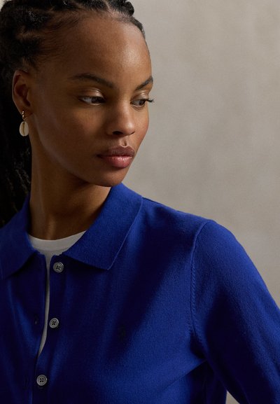 Μπλε πλεκτό πόλο πουκάμισο με γιακά, με πατιλέτα τριών κουμπιών και μικρή λεπτομέρεια με λογότυπο. Ομαλή υφή και εφαρμοστή γραμμή.