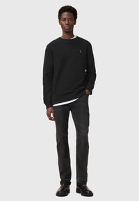 Black sweatshirt with round neck, ribbed cuffs, and a small logo. Paired with dark jeans and black boots, featuring a fitted design.