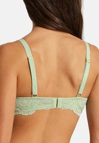 Soutien-gorge vert en dentelle avec des bretelles texturées et des éléments en or. La dentelle présente des motifs floraux, complétant le tissu lisse.