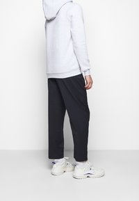 Felpa grigia chiara con cappuccio, abbinata a pantaloni larghi blu scuro. Sneakers bianchi con accenti blu. La texture sembra morbida e rilassata.