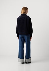 Chemise en velours côtelé bleu marine avec col, manches longues et détail de dos, associée à un jean en denim à jambes larges avec des poignets gris.