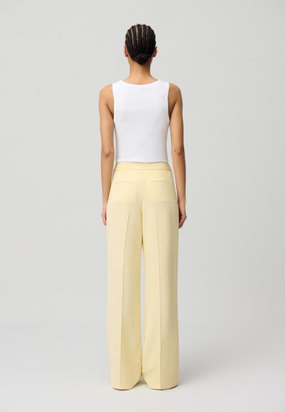 Un débardeur blanc et un pantalon large jaune, présentant une texture lisse et de légères poches arrière, vus de dos sur un fond neutre.