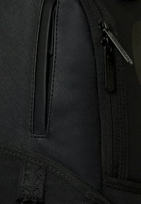 Mochila negra con un material sintético texturizado, bolsillo con cremallera y correas ajustables con costuras reforzadas.