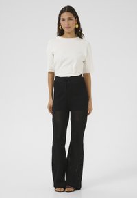 Witte relaxed-fit t-shirt en zwarte gebreide palazzo pants met een gestructureerde, open weving. De broek heeft een elastische tailleband met veters en wijde benen.