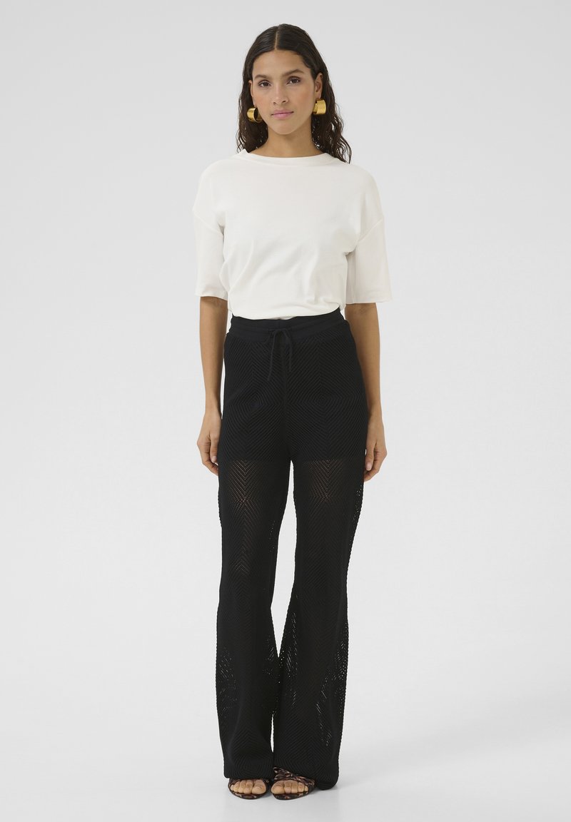 Witte relaxed-fit t-shirt en zwarte gebreide palazzo pants met een gestructureerde, open weving. De broek heeft een elastische tailleband met veters en wijde benen.