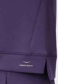 Purple athletic top with a soft texture, featuring a branded "VENICE BEACH" logo in white, and a side slit for ease of movement.