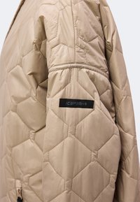 Manche de veste matelassée beige avec des coutures hexagonales et une étiquette noire indiquant "ICEPEAK" sur le haut du bras.