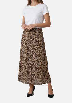 Donna che indossa una maglietta bianca a maniche corte, gonna midi marrone con stampa leopardata e bottoni sul davanti, e scarpe nere con tacco alto, in piedi con le mani intrecciate.
