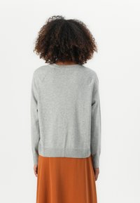 Grå genser med ribbestrikket kant og lange ermer, kombinert med et oransje skjørt. Designet har en enkel, jevn tekstur.