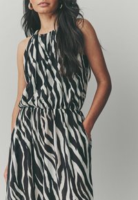 Vestido sin mangas de rayas zebra en blanco y negro con cintura elástica, que cuenta con bolsillos laterales y una textura de tela fluida.
