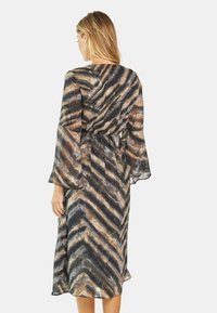 Durchsichtiges, langärmliges Kleid mit Zickzackmuster in Brauntönen, Schwarz und Grau; geraffte Taille, fließende Silhouette. Rückansicht dargestellt.