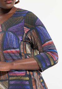 Schwarze Bluse mit einem lebendigen geometrischen Muster in Lila, Orange, Blau und Gelb, mit dreiviertel Ärmeln und einem V-Ausschnitt.