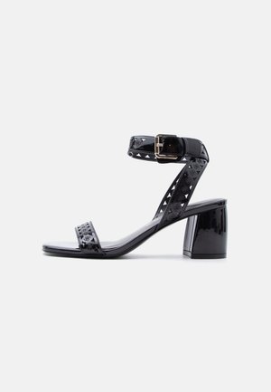 Schwarze Sandale aus lackiertem Leder mit Blockabsatz, Knöchelriemen und goldfarbenem Schnallenverschluss, mit dezent geprägtem Logomuster.