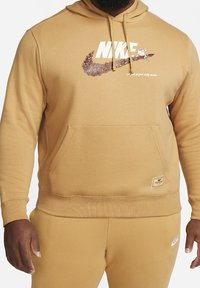 Pánská mikina s kapucí Nike v hnědé barvě. Obsahuje klokanku, velké logo s hnědou grafikou a kapuci na šňůrku. Hladká textura.