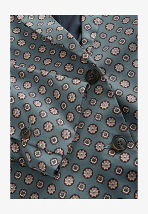 Vzorovaný sako v tyrkysové tkanině, s opakujícím se květinovým motivem v měděné a krémové barvě, s černými knoflíky a texturovaným povrchem.