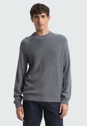 Grauer Langarmpullover mit gerippter Textur, Rundhalsausschnitt und Raglanärmeln. Getragen über dunklen Jeans aus Denim. Einfaches, einfarbiges Design.