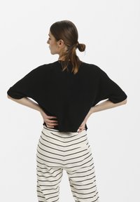 Čierny zkrátený sveter s klesnutými rukávmi, skombinovaný s krémovými nohavicami s horizontálnymi čiernymi pruhmi. Jednoduchý, textúrovaný úplet.