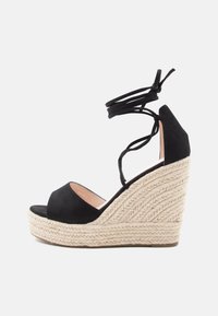 Schwarze Wildleder-Wedge-Sandalen mit einer geflochtenen Jute-Plattform, ausgestattet mit überkreuzten Knöchelriemen und einem offenen Zehendesign.