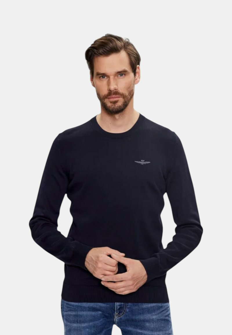 Navyblauwe gebreide trui met een ronde hals, geribbelde manchetten en zoom, met een subtiele logo op de borst. Gemaakt in combinatie met denim jeans.