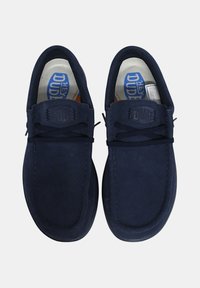 Zapatillas de ante azul de tipo slip-on con puntera redonda, cordones planos y plantilla de marca. Textura suave y diseño minimalista sin hardware visible.
