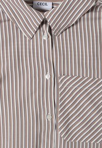 Chemise boutonnée avec des rayures verticales marron et blanches et une poche avant avec des rayures diagonales sous le col et une étiquette portant l'inscription "CECIL".