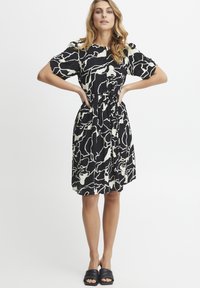 Vestido en blanco y negro con un patrón abstracto en espiral, mangas cortas abullonadas, cierre frontal de botones, cintura ceñida y falda hasta la rodilla.