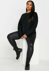 Mustat palmikkoneuleet, korkeavyötäröiset mustat legginsit ja mustat nauhalla varustetut taistelukengät, joissa on paksu pohja. Sileät tekstuurit ja tiukka siluetti.