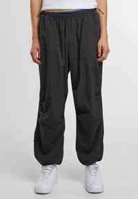 Zwarte lichtgewicht broek met elastische tailleband en trekkoord. Heeft een ontspannen pasvorm en zijzakken. Gecombineerd met witte sneakers.