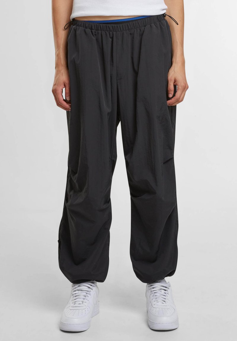 Zwarte lichtgewicht broek met elastische tailleband en trekkoord. Heeft een ontspannen pasvorm en zijzakken. Gecombineerd met witte sneakers.