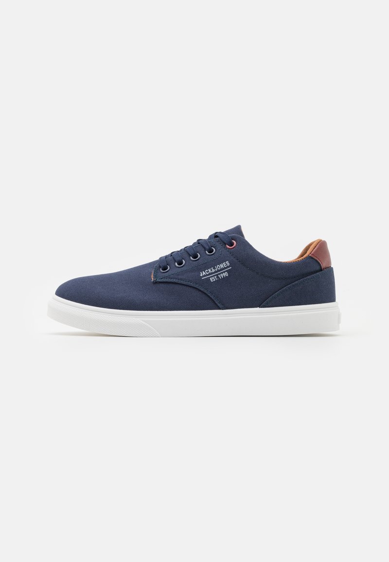 Navy canvas sneakers with white rubber sole, round toe, six eyelets, and brown accents on the heel. Features logo on the side.